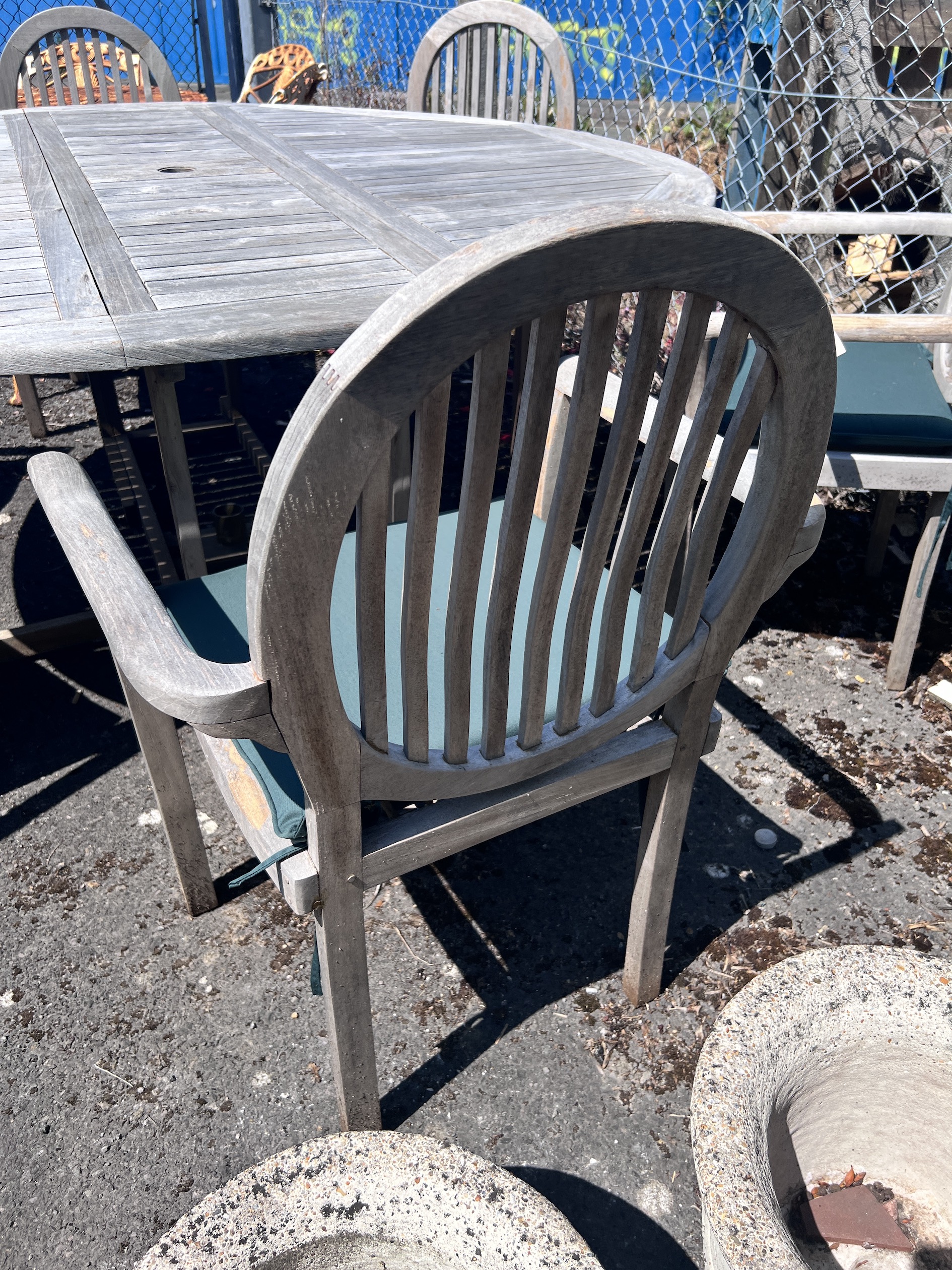 A circular weathered teak drop leaf garden table, 180cm extended, height 78cm, and six elbow chairs with seat cushions